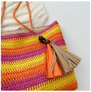 Detail of colorful striped straw tote bag with woven handles and paper tassel charm