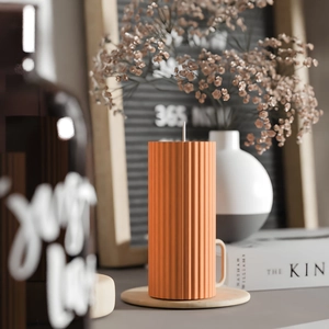 Modern orange pillar candle with vertical ribbed texture on a round wooden base tray