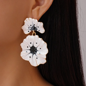 Close-up of enamel ginkgo flower drop earrings in black and white with gold edges