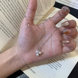 Minimalist silver necklace with three round pearls and zircon pendant held by hand