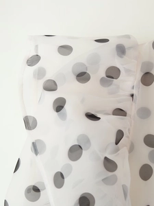 Close-up of white organza fabric with black polka dots and semi-transparent texture