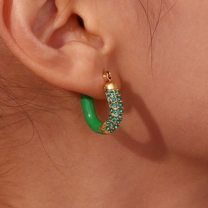 Macro view of C-shaped gold-plated earring with emerald zircons and green enamel finish
