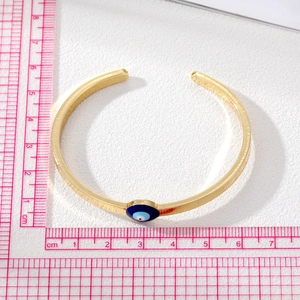 Golden open cuff bracelet with evil eye charm shown on a measurement scale