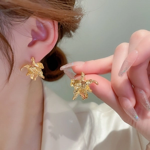 Macro detail of gold flower earrings with crumpled texture on a female model