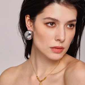 Modern oversized silver spherical stud earrings and geometric gold pendant necklace on model