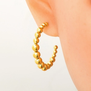 Macro shot of 18k gold-plated chunky bead hoop earrings on ear showing metallic luster