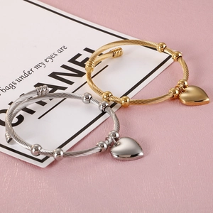 Gold and silver twisted steel open bracelets with heart pendants on a pink background