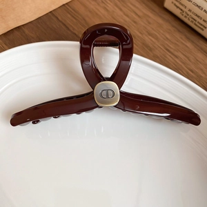 Detail of burgundy acrylic hair claw with vintage brass CD metal plate on ceramic tray