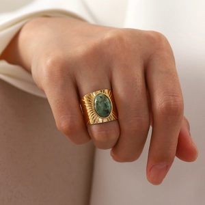 Close-up of vintage golden ring with oval green stone and sunburst texture on the finger
