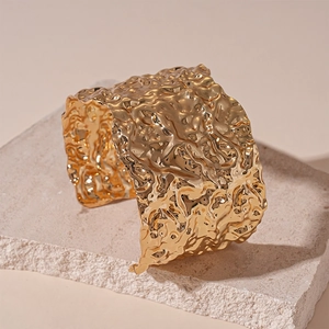 Detail of wide gold cuff bracelet featuring irregular lava texture on stone stand