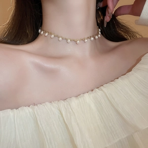 Close-up of elegant gold wave choker with hanging white pearls on model neckline