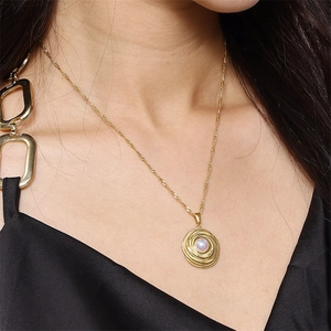 Detail of a spiral gold-plated pendant with a centered pearl worn by a model