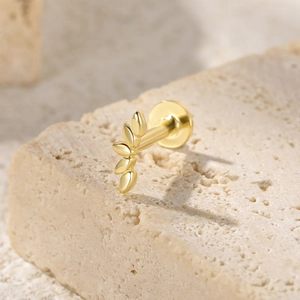 Macro shot of gold leaf earrings with screw backs on a textured beige stone base