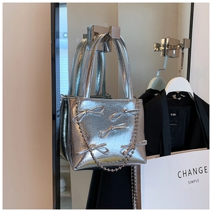 Detail of silver metallic handbag featuring ruffled texture, bows and a pearl chain strap