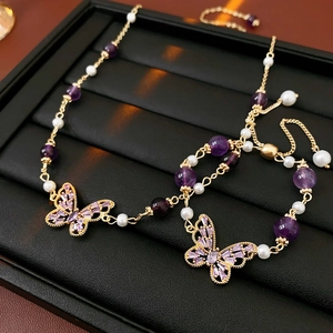 Close-up of jewelry set with purple butterfly charms, beads, and white pearls on a tray