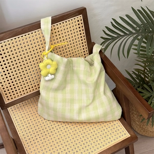 Detail of light green checkered canvas tote with a yellow flower charm on a rattan chair