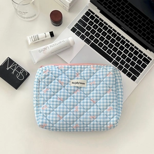 Detailed flat lay of quilted checkered makeup bag with bow pattern and zip closure