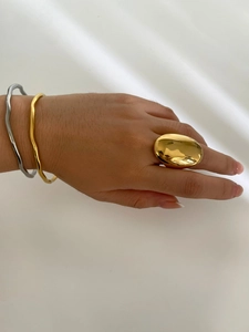 Polished gold oval ring and wavy metal bracelets styled on hand with soft shadows