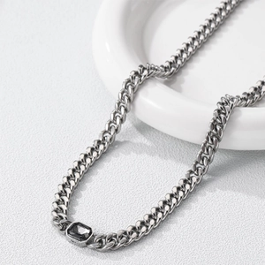 Silver Cuban link necklace with rectangular black gemstone on white ceramic display