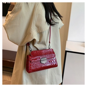 Detail of red crocodile pattern crossbody bag with metallic lock on trench coat model