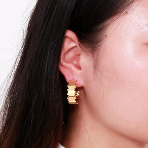 Gros plan de boucles d'oreilles dorées en forme de C avec texture d'engrenage étagé
