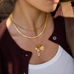 Detailed view of triple-layered gold necklaces with heart and daisy pendants on a model