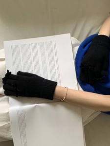 Close-up of black knitted fingerless gloves with bow detail held over an open book