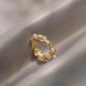Close-up of golden leaf ring with white pearls and zircons on grey silk background