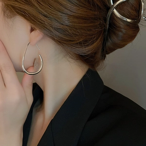 Close-up of woman wearing large polished silver teardrop earrings with mirror finish