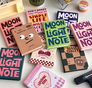 Overhead view of colorful A7 mini notebooks with cute cartoon illustrations and slogans