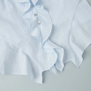 Detailed view of light blue cotton fabric with ruffle design and pearlescent buttons