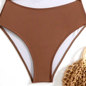 Detail van een bruin bikini-broekje met hoge taille, witte bies en strandtas van stro