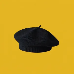 Detail of black knitted beret with a small stem top and ribbed edge on yellow background