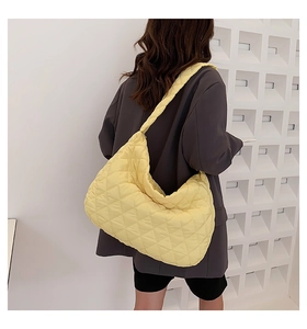 Detailed view of yellow quilted cloud shoulder bag worn by model against geometric wall