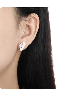 Close-up of irregular textured silver stud earrings with amber stones on a model's ear