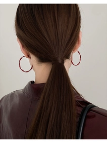 Detailed view of large dark red hoop earrings with matte finish on a female model