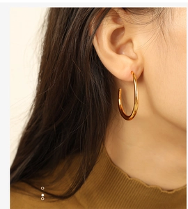 Close-up of elegant gold geometric hoop earrings worn by a model showing metal texture