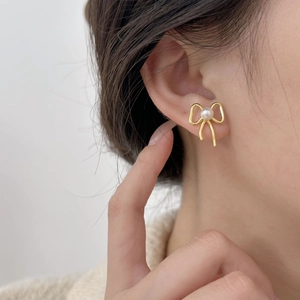 Elegant gold bow-shaped earrings with round white pearl on model, minimalist style
