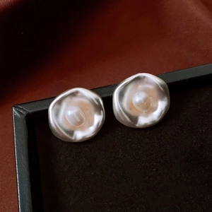 Primer plano de pendientes plateados irregulares con perla central estilo vintage.