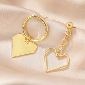 Close-up of asymmetric gold heart earrings featuring solid and hollow geometric pendants