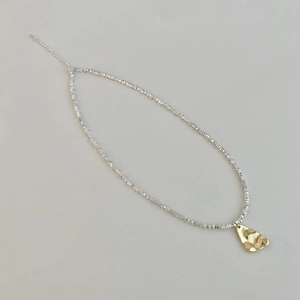 Detail of silver beaded chain with a golden hammered irregular pendant and extension