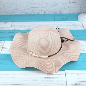 Detail of pink straw sun hat with pearl trim and black ribbon on a striped background