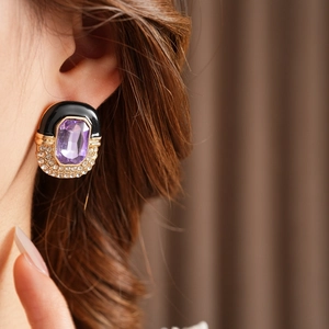 Detail of vintage square enamel earring with purple gemstone and gold accents on ear