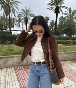 Detail shot of a brown suede cropped jacket featuring a lapel collar and metal zippers