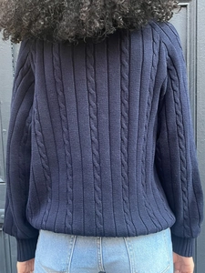 Detail view of navy blue cable knit sweater with ribbed hem and cuffs on dark wood background