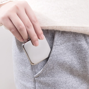Portable silver stainless steel folding pocket mirror being placed in a pants pocket