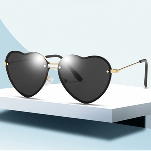 Fashion heart shaped sunglasses with gold metal frame and dark lenses on white podium