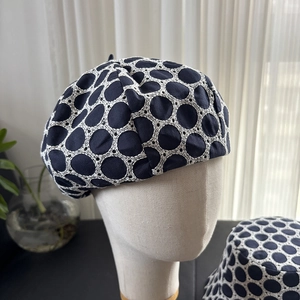 Detail of navy blue beret featuring white lace embroidery and hollow dot texture
