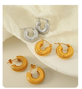Macro detail of ribbed gold and silver croissant hoop earrings on white fabric