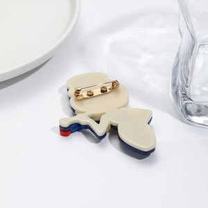 Modern acrylic cartoon brooch with gold metal safety pin back on minimalist white props